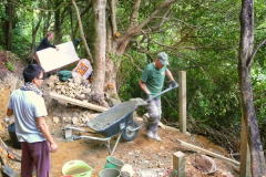 The upper kuti is much steeper; not such an easy site. Clare delivers floor insulation while John puts concrete in the foundations.