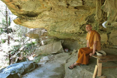 Ajahn Medhino sits under the broad cave-like overhang. Warm and dry.