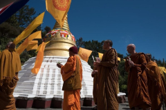 Under a clear sky the Sangha circumambulates the stupa.