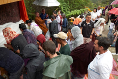The lay community add their treasures and blessings at the head of the buddha.