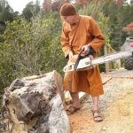 Ajahn Kusalo working on setting a post into the stump beside the quad track to hang a gate on.