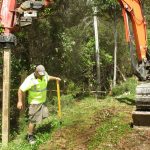 The first retaining wall post being driven in. Brian on the level Kevin in the digger.