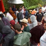 The lay community add their treasures and blessings at the head of the buddha.