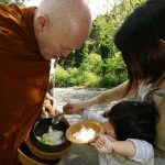 Ajahn Sucitto bending low for an offering of rice.