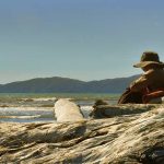 Venerable Kusalacitto between logs and sea and Kapiti Island.